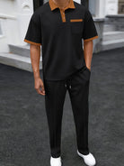 Person wearing a black and brown outfit with white shoes on a dark surface.