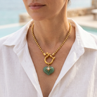 Woman wearing a green aventurine heart pendant necklace with a white linen blouse on a resort terrace.