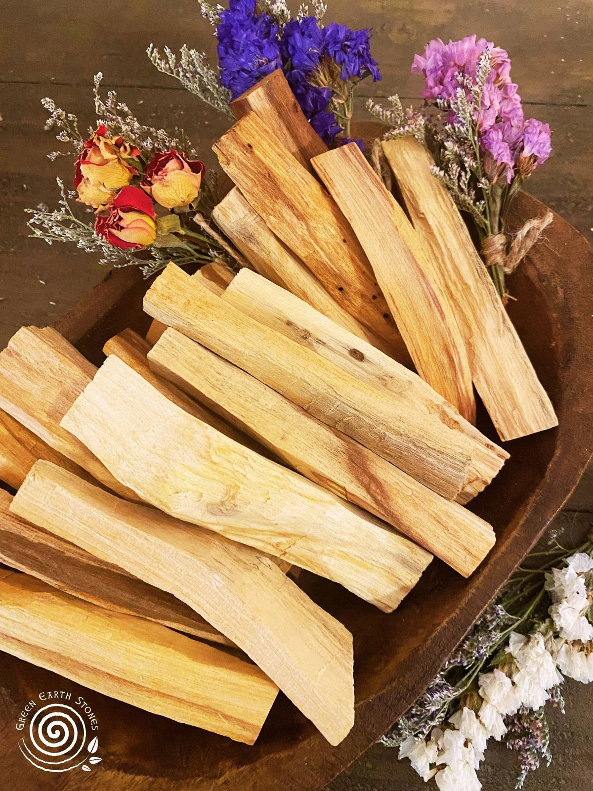 Palo Santo sticks in a wooden bowl with dried flowers on a wooden surface