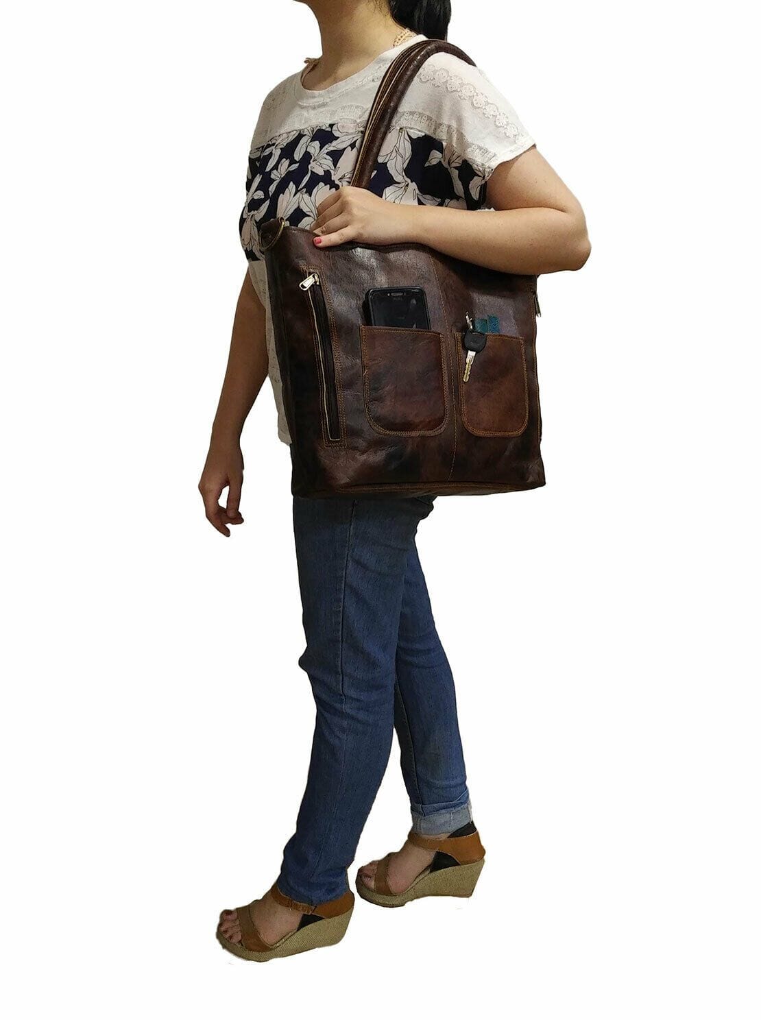 Person holding a brown leather backpack on a white background