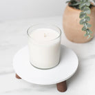 White candle in a glass holder on a white coaster with a plant in the background