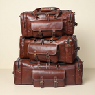 Three Traveler brown leather duffel sizes stacked against an ivory background, sold individually.